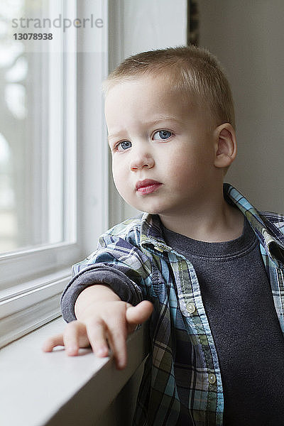 Porträt eines süßen Jungen  der zu Hause am Fenster steht