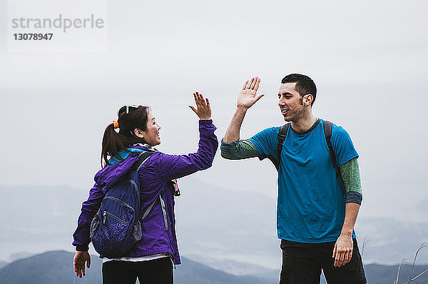 Freunde geben High-Five  während sie auf einem Berg vor klarem Himmel stehen