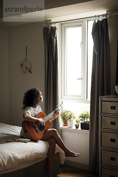 Frau schaut weg  während sie zu Hause Gitarre spielt