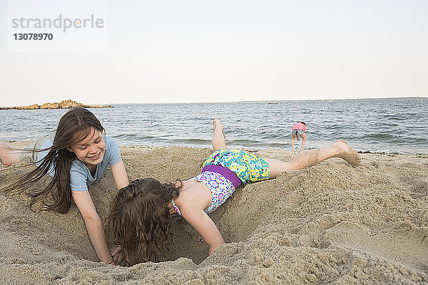 Schwestern spielen mit Sand am Strand gegen den klaren Himmel