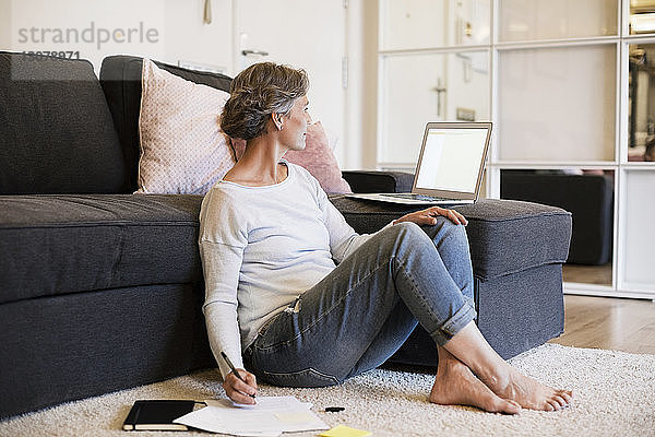 Reife Frau schreibt  während sie den Laptop im Wohnzimmer benutzt