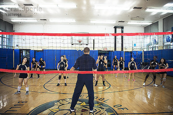Männlicher Trainer unterrichtet Übung für weibliche Volleyballmannschaft