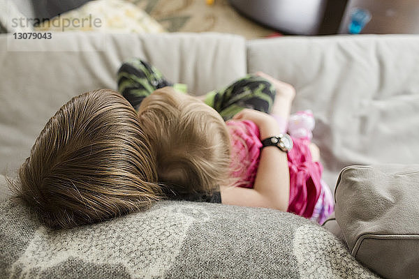 Schrägaufnahme eines Jungen  der seine Schwester umarmt  während er sich zu Hause auf dem Sofa entspannt