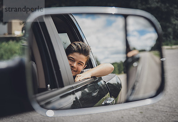 Spiegelung eines fröhlichen Jungen im Seitenspiegel am Auto gesehen