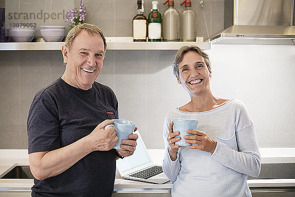 Porträt eines glücklichen älteren Ehepaares mit Kaffeebechern in der Küche