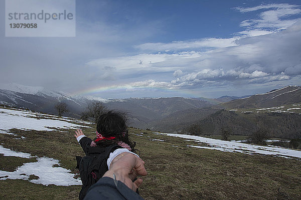 Ausgeschnittenes Bild eines Freundes  der im Winter die Hand einer Frau gegen Berge und Regenbogen hält