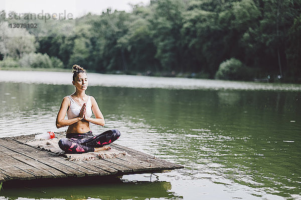 Frau meditiert  während sie am Pier über einem See im Wald sitzt