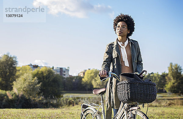 Nachdenkliche Frau mit Fahrrad steht auf dem Feld vor klarem Himmel