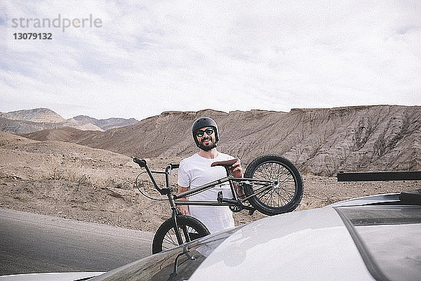 Porträt eines Mannes  der ein Fahrrad auf ein Auto lädt  vor Bergen und bewölktem Himmel