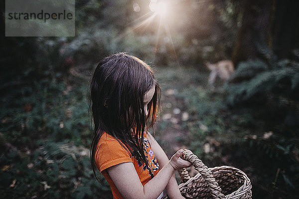 Seitenansicht eines im Wald stehenden Mädchens mit Weidenkorb