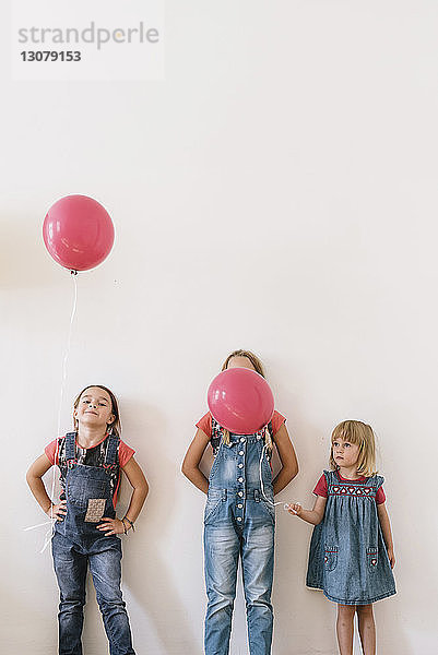 Schwestern mit Luftballons stehen zu Hause an der Wand