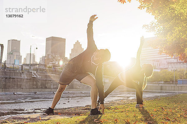 Paar praktiziert Yoga im Park bei Sonnenaufgang