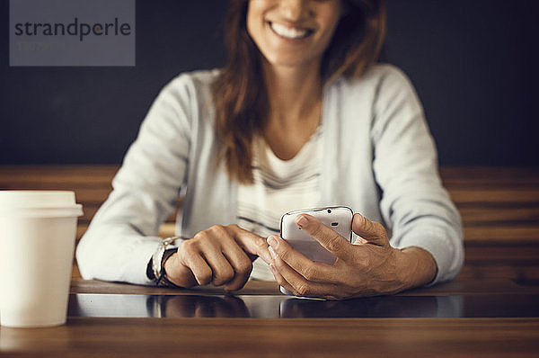 Mitschnitt einer lächelnden Frau  die im Café ein Mobiltelefon benutzt