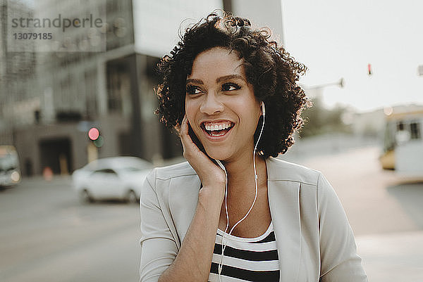 Glückliche Frau schaut weg  während sie auf der Straße Musik hört
