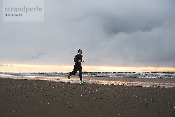 Mann joggt am Strand gegen bewölkten Himmel