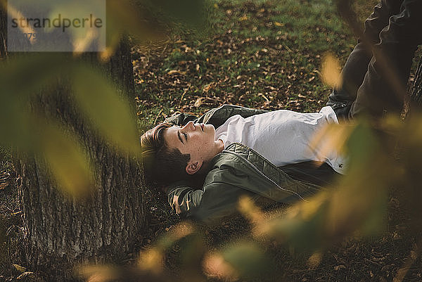 Hochwinkelansicht eines nachdenklichen Jungen  der im Park liegt  durch Zweige gesehen