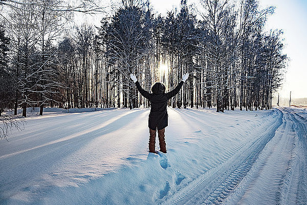 Rückansicht einer Frau  die mit erhobenen Armen auf einem schneebedeckten Feld steht