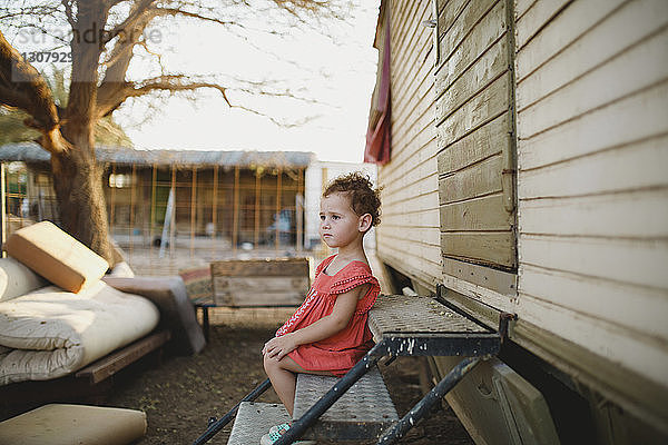 Seitenansicht eines süßen Mädchens  das weg schaut  während es auf Metallstufen auf einem Bauernhof sitzt