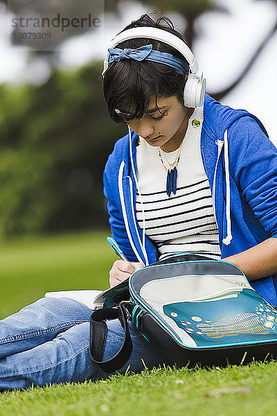 Teenager-Mädchen hört Musik  während sie im Park an einem Tagebuch schreibt