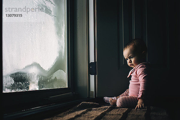 Kleines Mädchen sitzt zu Hause an einer Tür aus beschlagenem Glas