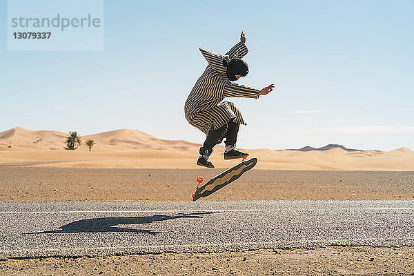 Seitenansicht eines Mannes  der beim Skateboardfahren auf der Straße gegen den Himmel springt