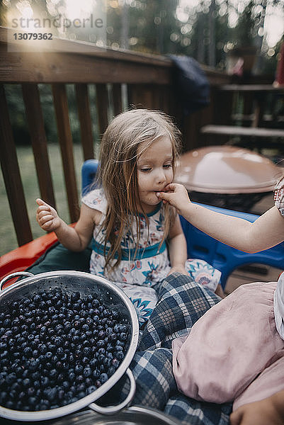 Ausgeschnittenes Bild eines Mädchens  das seine Schwester auf der Veranda mit Blaubeeren füttert