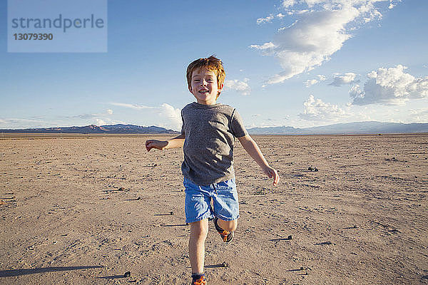 Porträt eines glücklichen Jungen  der auf einer trockenen Landschaft läuft