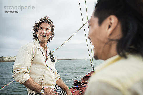 Glücklicher Mann schaut weg  während er mit einem Freund auf einem Segelboot reist