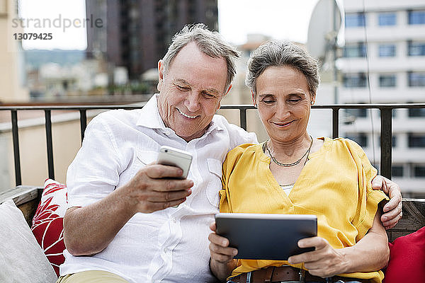 Glückliches älteres Paar mit Smartphone und Tablet-Computer auf der Terrasse