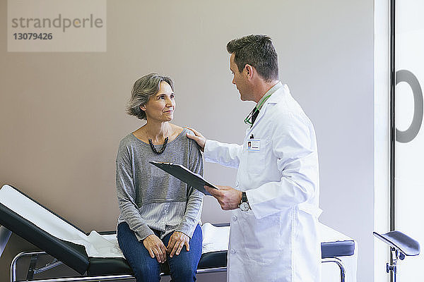 Lächelnder Patient im Gespräch mit dem Arzt  während er im Krankenhaus am Bett sitzt