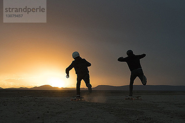 Rückansicht von Freunden  die bei Sonnenuntergang gegen den Himmel skateboarden
