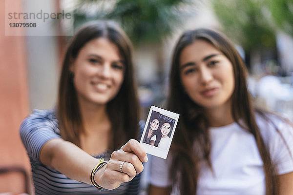 Porträt von Freunden  die ein Sofortbild zeigen  während sie im Straßencafé sitzen