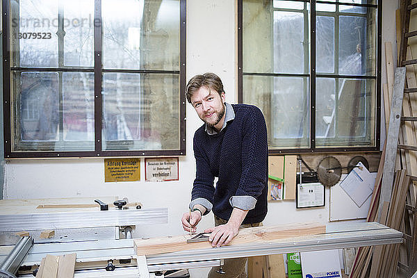 Portrait eines Tischlers beim Vermessen von Holzbohlen in der Werkstatt