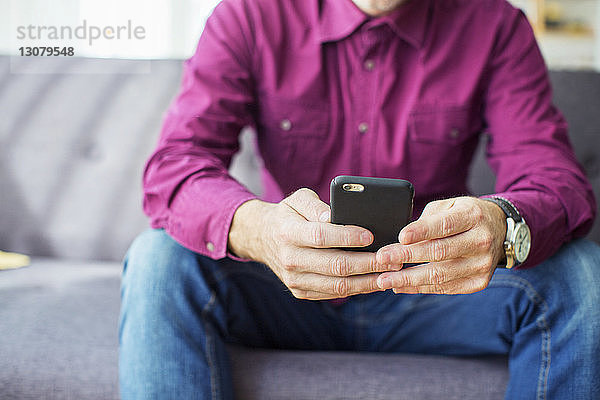 Mittelsektion eines Geschäftsmannes  der im Büro ein Mobiltelefon auf dem Sofa benutzt