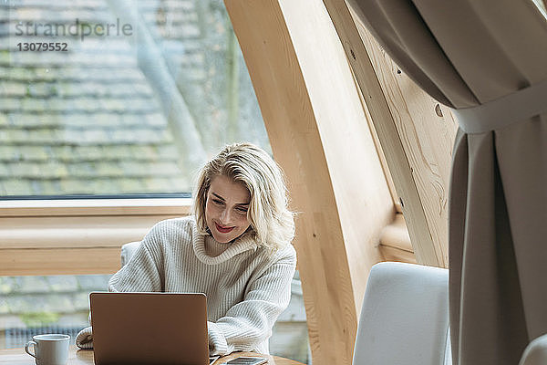 Frau benutzt Laptop-Computer  während sie zu Hause am Fenster sitzt