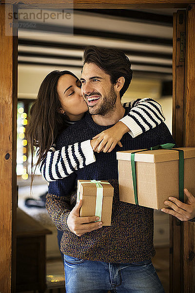 Frau küsst ihren Freund mit Geschenkkartons an der Tür