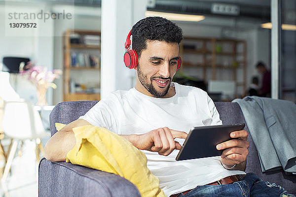 Geschäftsmann benutzt Tablet-Computer  während er sich im Büro auf dem Sofa entspannt