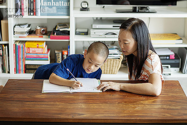 Schrägaufnahme einer Mutter  die ihrem Sohn bei den Hausaufgaben hilft  während er zu Hause sitzt