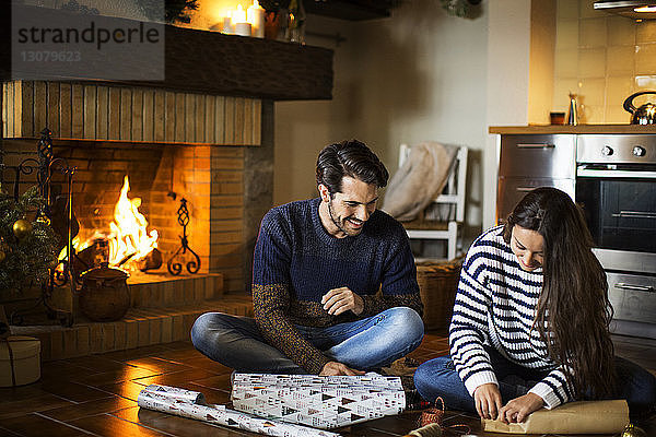 Glückliches Paar packt Geschenkkartons auf dem Boden am heimischen Kamin ein