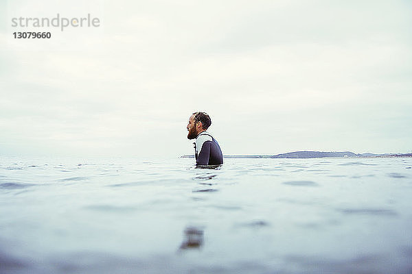 Seitenansicht eines männlichen Surfer im Meer vor bewölktem Himmel
