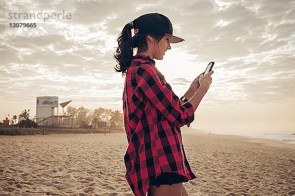 Junge Frau schreibt am Strand SMS