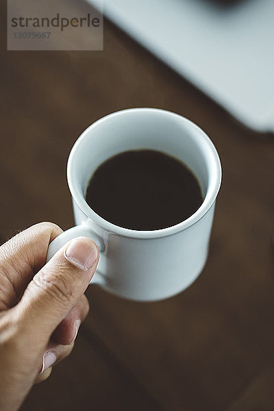 Abgehackte Hand eines Mannes  der zu Hause eine Kaffeetasse über den Tisch hält