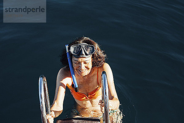 Hochwinkelansicht einer glücklichen Frau  die die Leiter eines Bootes auf dem Meer erklimmt