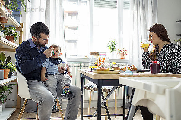 Frau betrachtet Ehemann  der seinen Sohn am Tisch in der Küche füttert