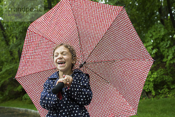 Lachendes Mädchen mit Regenschirm in der Hand im Park