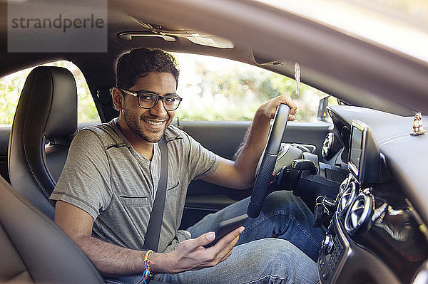 Porträt eines lächelnden Mannes mit Handy im Auto unterwegs