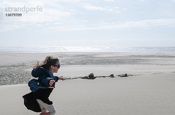 Seitenansicht eines Mädchens mit ausgestreckten Armen  das am Strand gegen den Himmel rennt