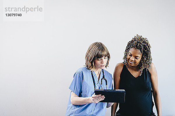 Ärztin zeigt schwangere Frau Ultraschall am Tablet-Computer  während sie vor weissem Hintergrund sitzt