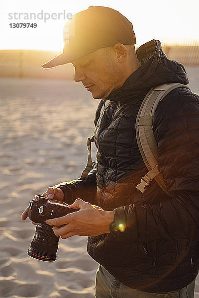 Mann mit Kamera steht bei Sonnenuntergang am Strand vor klarem Himmel