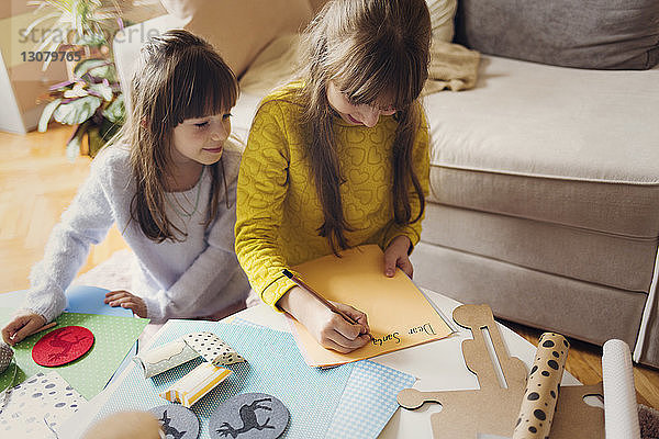 Lächelndes Mädchen von Schwester schreibt bei Tisch auf Papier